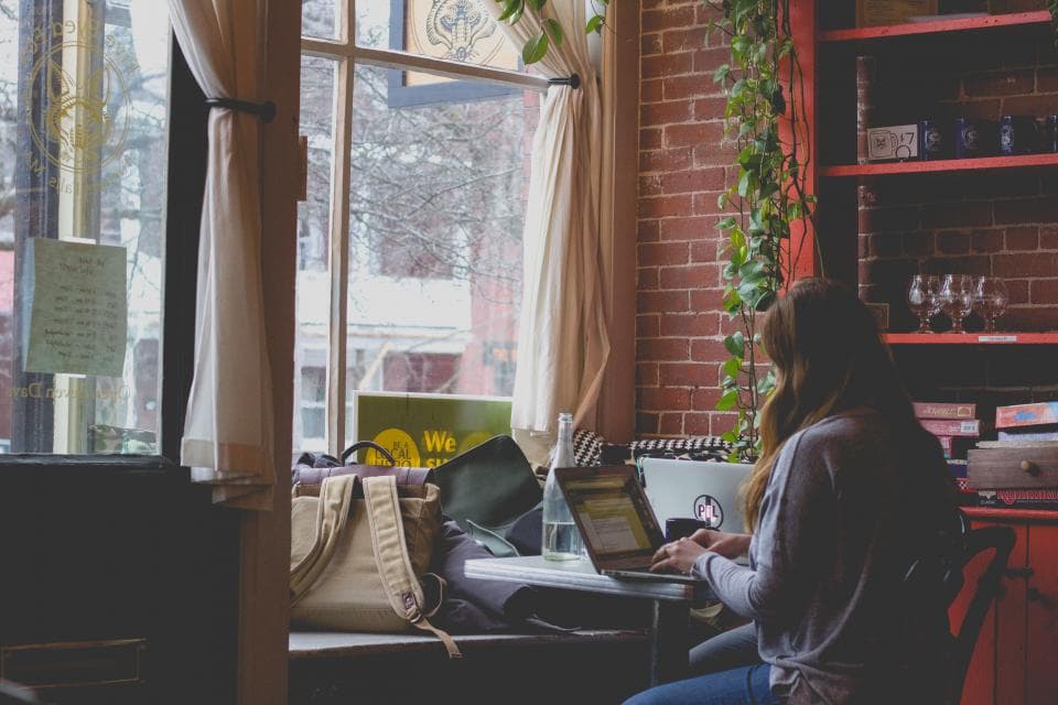 Someone working on a laptop by a warm café window